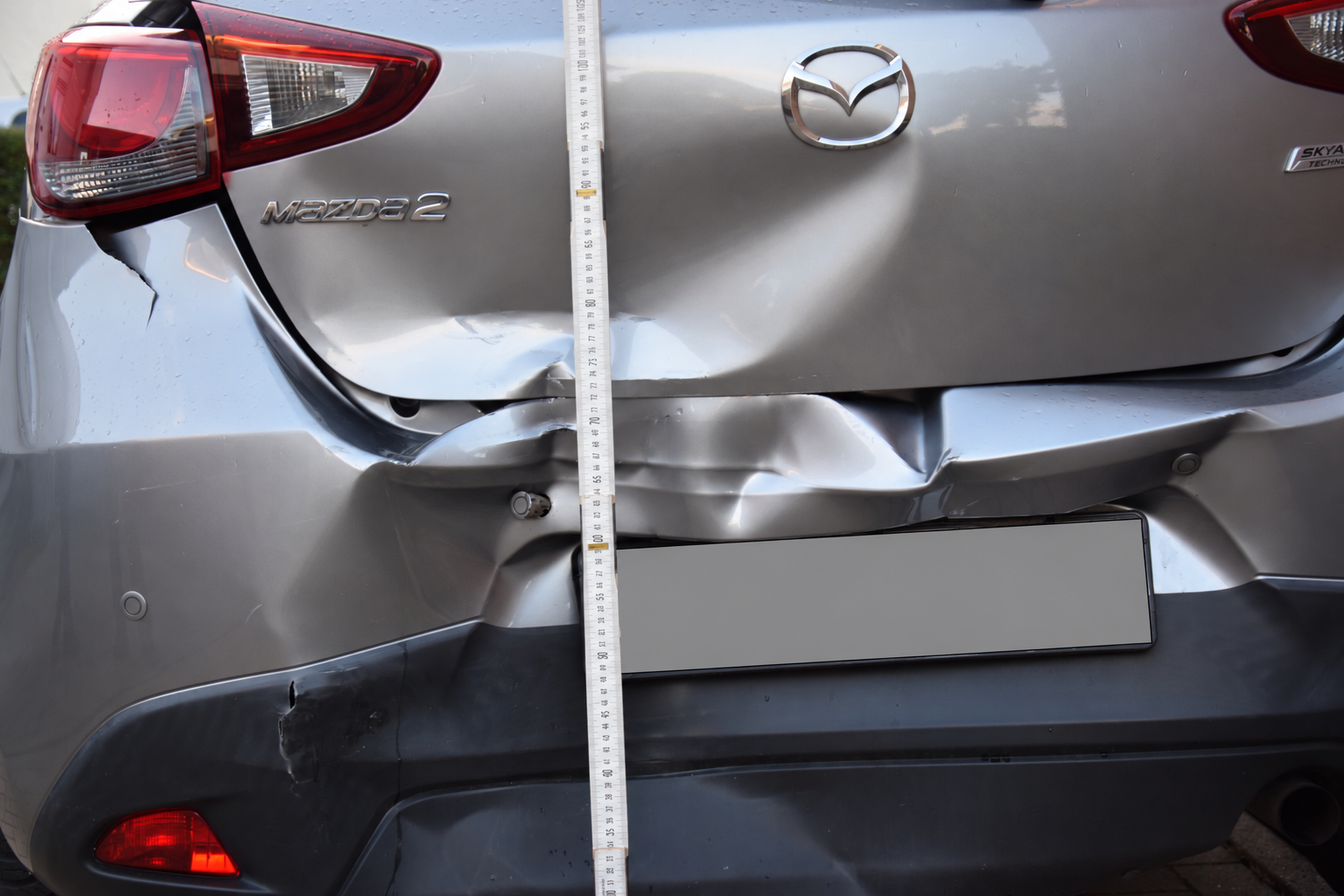 Heckschaden am selben Mazda 2 mit verformter Heckklappe und Stoßfänger; Kennzeichen verdeckt.